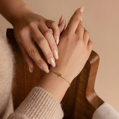 Close-up of a hand wearing a gold bracelet with another hand gently touching it against a warm-toned background.