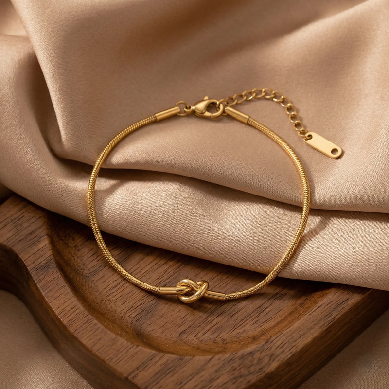 Gold bracelet with a knot design on a beige fabric background