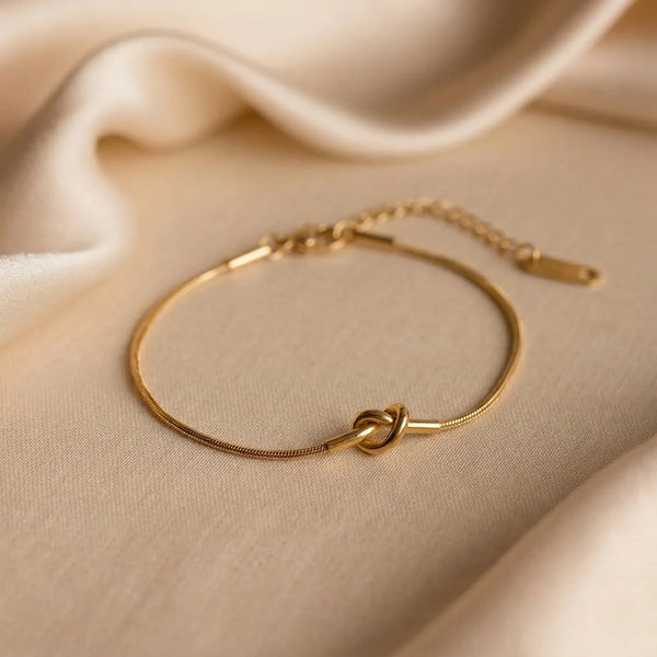 Gold bracelet with a knot design on a beige fabric background