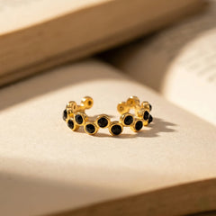 Gold hoop earrings with black gemstones on a beige surface