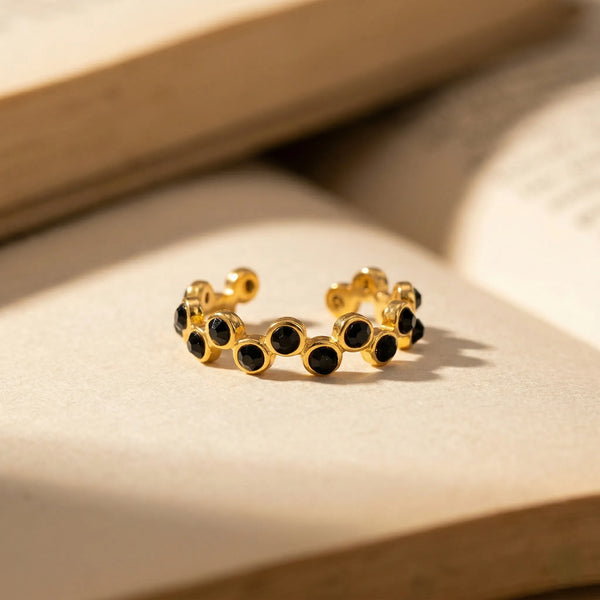 Gold hoop earrings with black gemstones on a beige surface